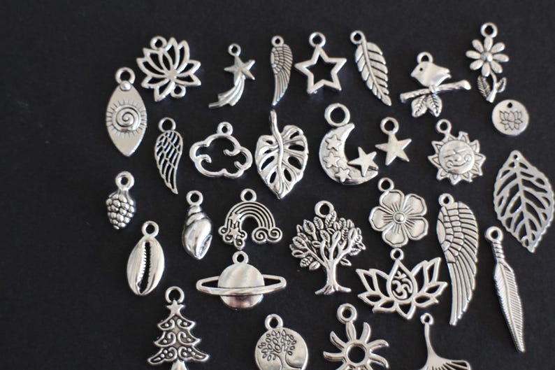 May include: A collection of silver charm pendants featuring various designs, including leaves, stars, moons, clouds, flowers, and more. These charms are perfect for adding a personal touch to jewelry projects.