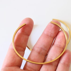 Könnte beinhalten: Zwei goldfarbene Metallarmbänder, eines etwas größer als das andere, werden in einer Hand gehalten. Die Armbänder sind schlicht und haben eine glatte, polierte Oberfläche.