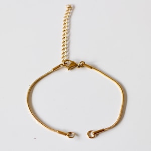 Könnte beinhalten: Ein goldenes Kettenarmband mit einem Karabinerverschluss.