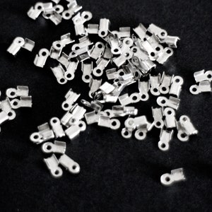 May include: A pile of silver-toned metal crimp beads, used for jewelry making.