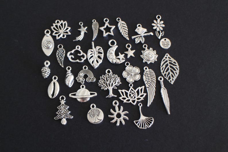 May include: A collection of 28 silver charm pendants featuring various designs, including stars, moons, leaves, flowers, animals, and symbols. The charms are perfect for jewelry making, scrapbooking, and other craft projects.