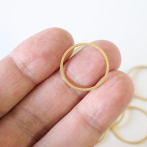 Può includere: Una collezione di sottili anelli metallici circolari color oro. Ogni anello presenta una superficie liscia e piatta con un design semplice e aperto. Questi piccoli componenti metallici leggeri sono di forma circolare e hanno una finitura dorata.