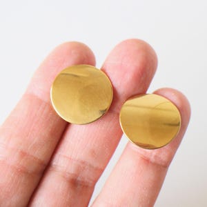 Puede incluir: Un par de pendientes redondos de color dorado. Los pendientes son simples y minimalistas en diseño.