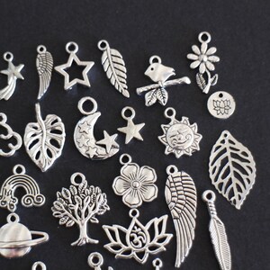 May include: A collection of silver charm pendants featuring various designs, including leaves, flowers, stars, moons, clouds, wings, and a rainbow. The charms are perfect for jewelry making or crafting.