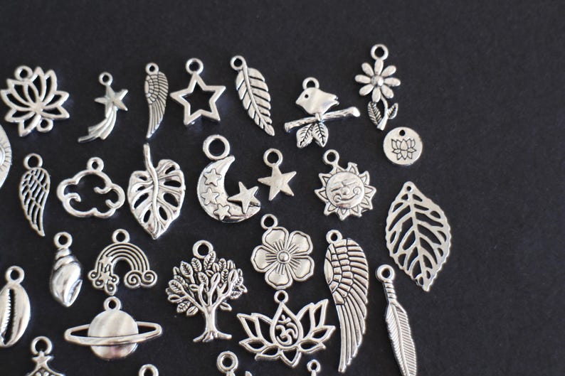 May include: A collection of silver charm pendants featuring various designs, including leaves, flowers, stars, moons, clouds, wings, and a rainbow. The charms are perfect for jewelry making or crafting.