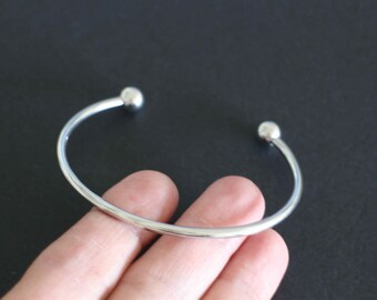 Un bracelet jonc épais ouvert en acier inoxydable argent de 17 cm dont une boule peut se dévisser pour l'agrémenter selon vos envies