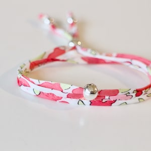 May include: A pink and white floral fabric bracelet with silver beads. The bracelet is adjustable with a sliding knot.