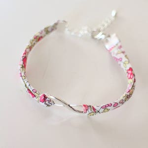 Puede incluir: Un brazalete de tela blanca con un patr&oacute;n floral rosa y un cierre de plata en forma de infinito.