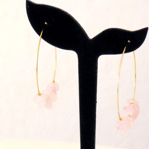 Op de afbeelding: Gouden creolen met roze rozenkwartsstenen die aan de onderkant hangen.