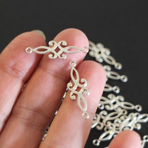 Puede incluir: Encantos de conector de filigrana plateada con dos bucles a cada lado. Los encantos tienen la forma de un diseño floral estilizado.
