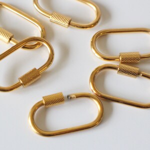 May include: Six gold-toned metal oval-shaped keychains with a threaded screw closure.