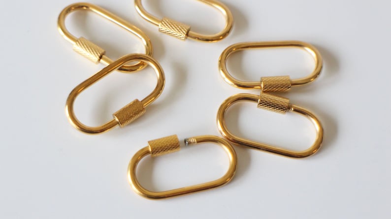 May include: Six gold-toned metal oval-shaped keychains with a threaded screw closure.