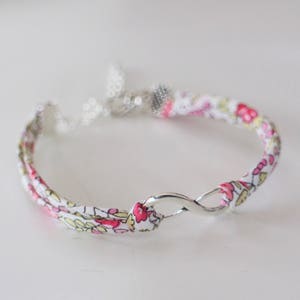 Puede incluir: Un brazalete de tela blanca con un estampado floral rosa y amarillo y un cierre de s&iacute;mbolo de infinito plateado.