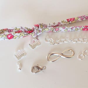 Puede incluir: Una colecci&oacute;n de suministros de fabricaci&oacute;n de joyas plateados, que incluyen una cadena, un amuleto de infinito, anillos de salto y cierres. Tambi&eacute;n hay un trozo de tela con un patr&oacute;n floral.