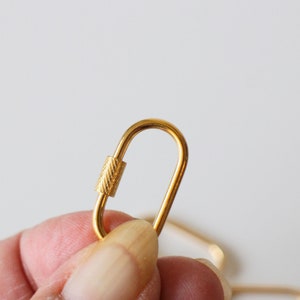May include: A gold-colored metal lobster clasp with a textured finish. The clasp is open and ready to be attached to a chain or other jewelry.