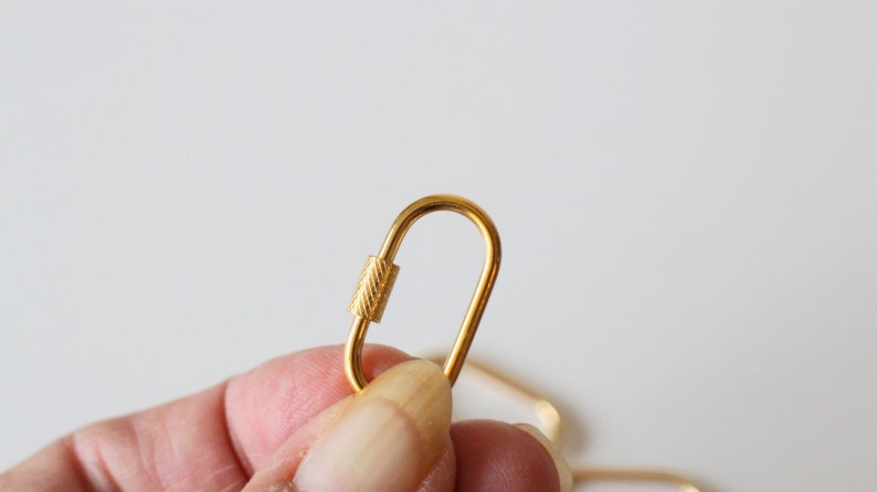 May include: A gold-colored metal lobster clasp with a textured finish. The clasp is open and ready to be attached to a chain or other jewelry.
