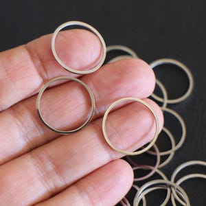 Puede incluir: Una colección de anillos metálicos finos y circulares en tono plateado. Estos anillos pequeños, lisos y ligeros presentan un diseño sencillo y sin adornos con una forma redonda constante, presentados como un grupo de varias piezas de joyería.