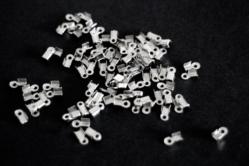 May include: A pile of silver metal crimp end caps for jewelry making.