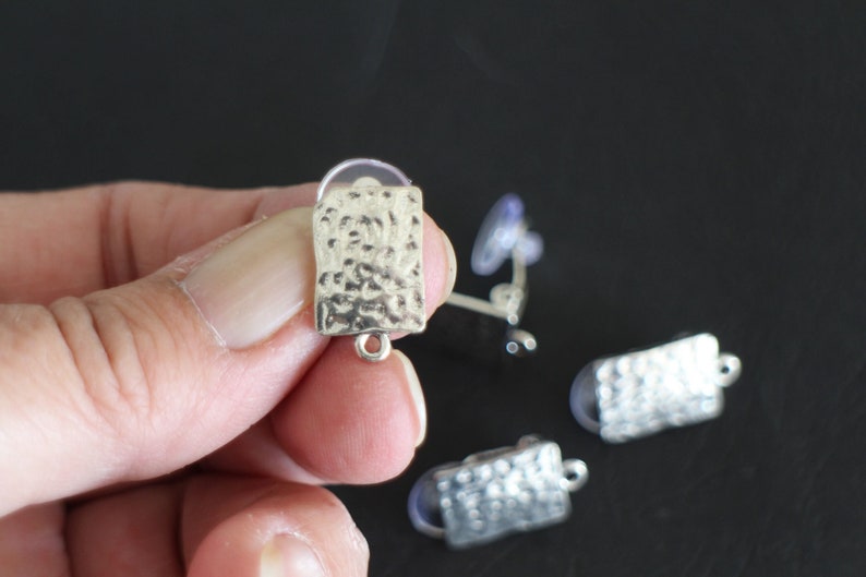 May include: Silver-toned earring findings with a hammered texture and a loop for attaching a pendant. The findings are shown on a black surface.