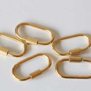 May include: Five gold-colored oval-shaped keychains with a textured metal ring. Each keychain has a small, textured metal cylinder in the center.