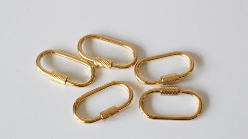 May include: Five gold-colored oval-shaped keychains with a textured metal ring. Each keychain has a small, textured metal cylinder in the center.