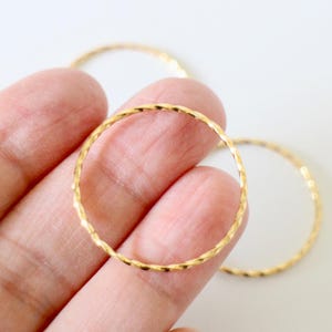 Pode incluir: Close-up de três anéis de metal dourado texturizado. Os anéis são circulares com uma superfície texturizada. Os anéis estão em um fundo branco. Os anéis são segurados por uma mão.