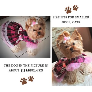 May include: A small dog wearing a pink and black plaid dress with a pink tulle skirt and white lace trim. The dog is about 5.3 lbs or 2.4 kg. The text "SIZE FITS FOR SMALLER DOGS, CATS" is at the top of the image.