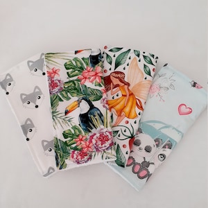 May include: Four fabric squares with different designs. One square has a white background with grey fox faces. Another square has a white background with a toucan, tropical leaves, and pink flowers. A third square has a green background with a fairy with wings and a yellow dress. The last square has a light blue background with a panda bear and pink flowers.