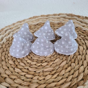 Puede incluir: Seis conos de tela gris con estrellas blancas impresas en ellos. Los conos están dispuestos en círculo sobre una estera de paja tejida.