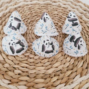 May include: Six white fabric cone-shaped reusable makeup remover pads with a panda bear print. The pads are on a woven straw mat.