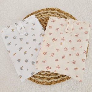 Puede incluir: Dos cuadrados de tela con un patrón floral. Un cuadrado es blanco con flores azules y el otro es beige con flores rosas. Ambos cuadrados tienen un cierre de botón.