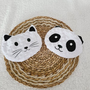 May include: Two white plush toys with black embroidered faces. The toy on the left is a cat with white whiskers and the toy on the right is a panda with black eyes and a black nose.