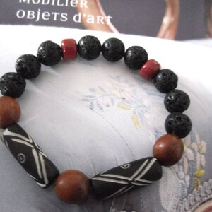 May include: A black lava rock bracelet with red and brown wooden beads. The bracelet features two black and white patterned beads.