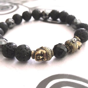 Peut inclure: Un bracelet en perles de roche volcanique noire et d'hématite avec un pendentif en forme de tête de Bouddha dorée et une perle d'onyx noire.
