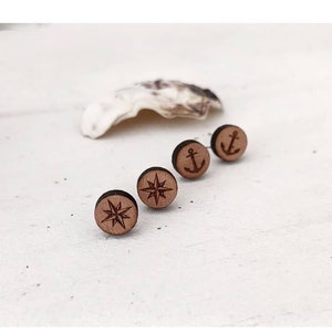 Puede incluir: Cuatro pendientes de madera con diseños náuticos. Los pendientes presentan una brújula, un ancla y dos diseños de brújula.