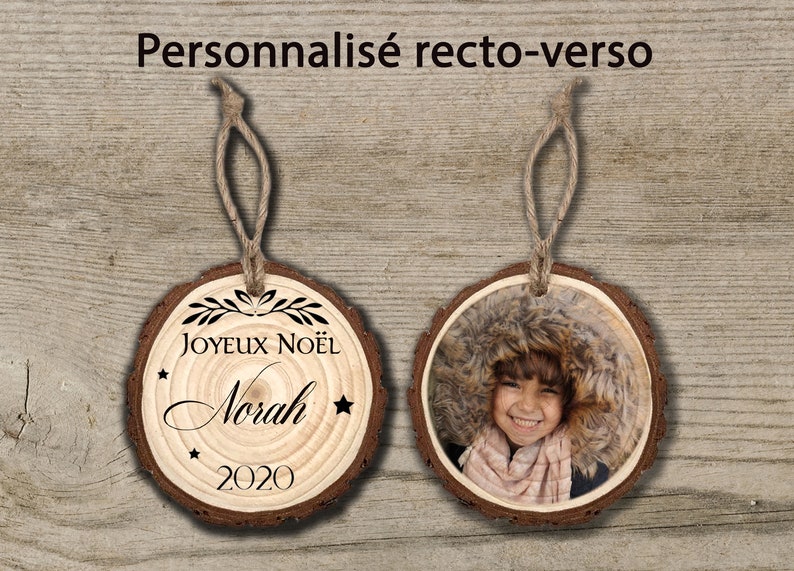 May include: A personalised wooden Christmas bauble with a photo on one side and the text "Joyeux No&euml;l Norah 2020" on the other side.