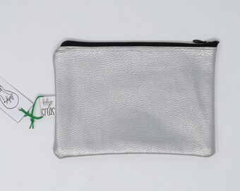 Può includere: Una pochette argentata con cerniera a zip nera e un'etichetta bianca con la scritta "lelye creas".