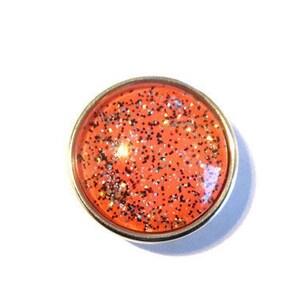 May include: A round, orange glitter snap with a silver metal rim.