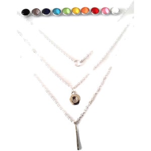 Puede incluir: Un collar de plata de varias capas con tres cadenas, que incluye un pequeño círculo, un colgante circular y una barra vertical. Arriba, una fila de botones de presión redondos y coloridos: negro, gris, azul, turquesa, verde, amarillo, naranja, rojo, rosa y blanco.
