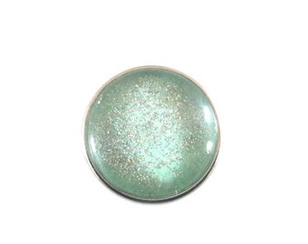 18mm glass cabochon press button with silver glitter on a green background.