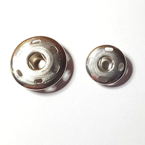 Peut inclure: Deux boutons-pression en métal argenté, l'un plus grand que l'autre, sur un fond blanc.