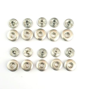 May include: A set of 15 silver metal snap buttons. The buttons are round and have a raised center. They are arranged in three rows of five.