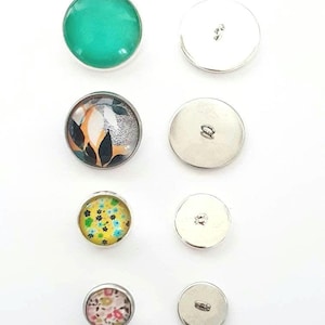 Peut inclure: Assortiment de huit boutons, dont six boutons en métal argenté et deux boutons en verre avec des motifs colorés. Les boutons en verre présentent un motif vert, floral et à motifs.