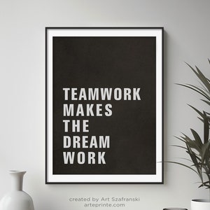Puede incluir: Póster motivacional en blanco y negro con el texto "TEAMWORK MAKES THE DREAM WORK" sobre un fondo negro. El póster está enmarcado en un marco negro fino y está colgado en una pared blanca.