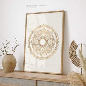 May include: A framed print of a gold mandala design on a white background. The print is displayed on a wooden shelf with a vase of dried branches and a wooden beaded necklace.