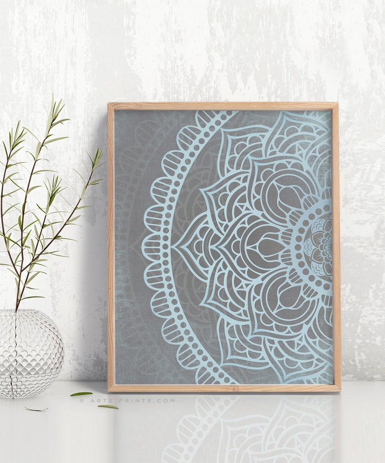 Puede incluir: Una impresi&oacute;n enmarcada de un dise&ntilde;o de mandala azul y gris. El mandala es un patr&oacute;n circular con intrincados detalles. La impresi&oacute;n est&aacute; enmarcada en un marco de madera claro.