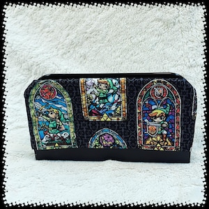 May include: A black rectangular case with a stained-glass design featuring a video game character. The stained-glass panels are in shades of blue, red, green, and yellow. The case has a black base and a black top.