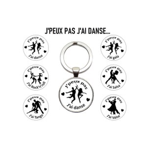 Peut inclure: Un porte-clés argenté avec un charme rond en verre représentant une silhouette noire d'un couple dansant. Le charme porte le texte "J'peux pas J'ai danse" en français, ce qui se traduit par "Je ne peux pas, je danse".