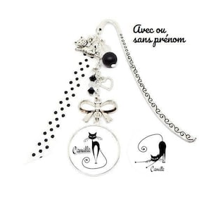 Peut inclure: Signet noir et blanc avec un charme de chat argenté, un nœud argenté et des perles noires. Le signet a un cercle blanc avec un chat noir et le texte "Camille" dessus. Le signet a également une chaîne argentée avec un charme en forme de cœur. Le texte "Avec ou sans prénom" est écrit sur le signet.
