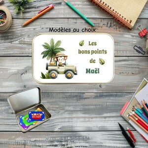 Peut inclure: Une boîte métallique rectangulaire avec un couvercle illustré d'un singe en jeep de safari, de palmiers et du texte "Modèles au choix" et "Les bons points de Maël". Une boîte ouverte en dessous contient des petites cartes rectangulaires colorées.